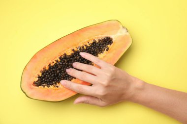 Sarı arka planda papaya 'nın yarısına dokunan genç bir kadın. Seks konsepti