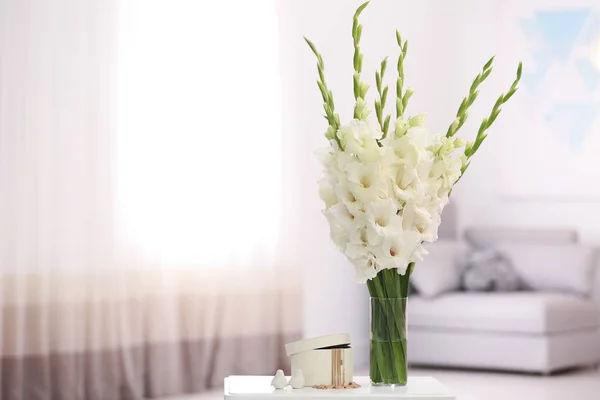 Vas dengan bunga gladiolus putih yang indah dan perhiasan di atas meja kayu di kamar, ruang untuk teks — Stok Foto