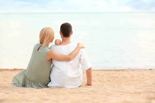 Pareja romántica feliz sentados juntos en la playa, espacio para el texto — Foto de Stock
