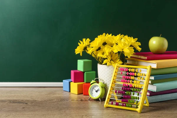 Vaso de flores, livros e brinquedos em mesa de madeira perto de quadro-negro verde, espaço para texto. Dia do professor — Fotografia de Stock
