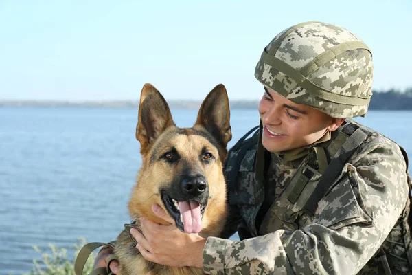 Hombre en uniforme militar con perro pastor alemán cerca del río — Foto de Stock