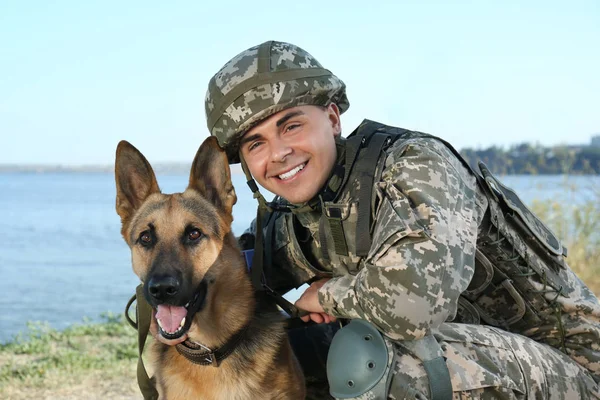 Hombre en uniforme militar con perro pastor alemán cerca del río — Foto de Stock