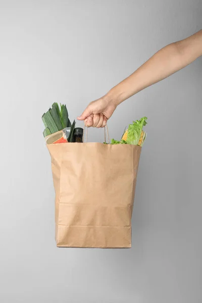 Woman holding paper bag with fresh vegetables on grey background, closeup