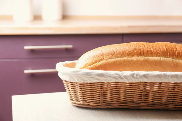Weidenkorb mit einem Laib leckerem frischem Brot auf Holztisch in der Küche — Stockfoto