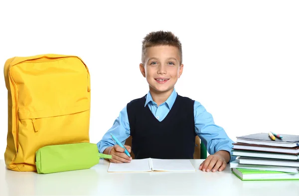 Liten pojke i uniform gör uppdrag vid skrivbordet mot vit bakgrund. Skol brevpapper — Stockfoto