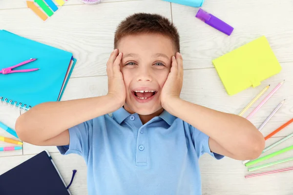 Emotionaler kleiner Junge mit Schulpapier auf Holzgrund, Draufsicht — Stockfoto