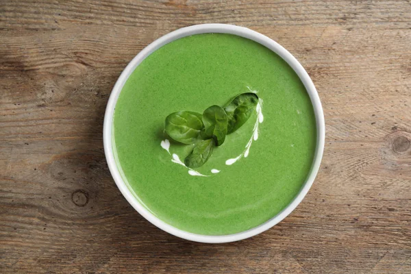 Bol de soupe verte saine aux épinards frais sur table en bois, vue sur le dessus — Photo