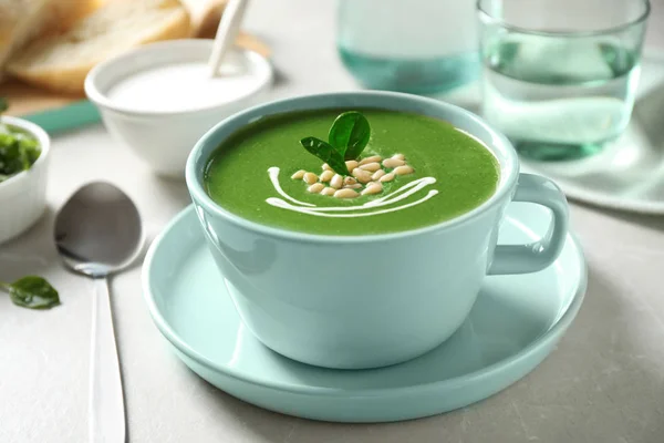 Cup of healthy green soup with fresh spinach on light table