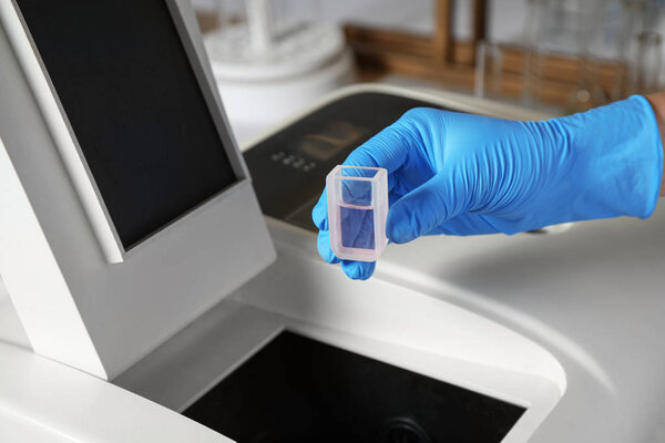 Scientist putting sample compartment with liquid in spectrophotometer, closeup. Laboratory analysis