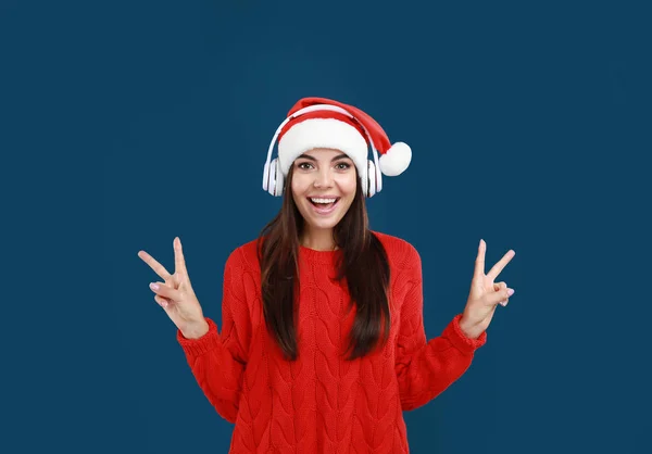 Mujer joven en Santa Sombrero escuchando música navideña sobre fondo azul oscuro —  Fotos de Stock