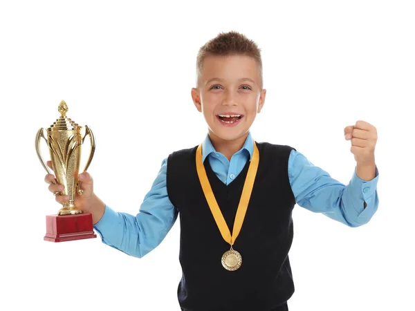 Ευτυχισμένο αγόρι με σχολική στολή με χρυσό κύπελλο και μετάλλιο απομονωμένο σε λευκό — Φωτογραφία Αρχείου