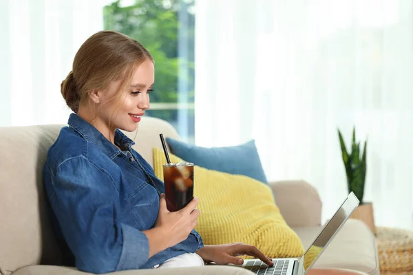 Young woman with glass of cola working on laptop at home. Refreshing drink — Stock Photo, Image