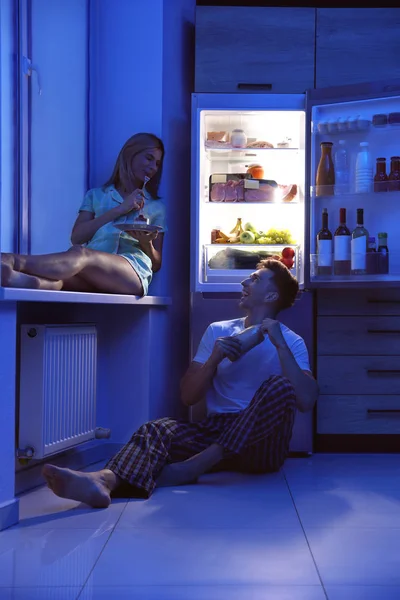 Happy para jedzenia w pobliżu lodówki w kuchni w nocy — Zdjęcie stockowe