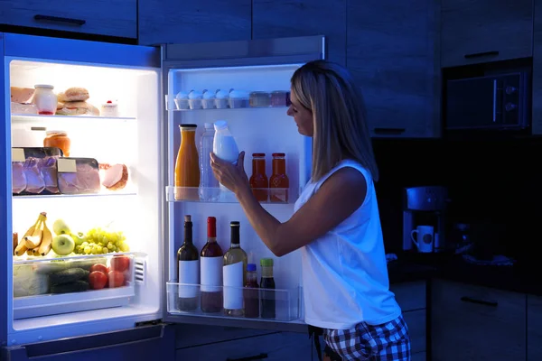 Žena brát láhev s mlékem z chladničky v kuchyni v noci — Stock fotografie