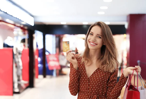 Glad ung kvinna med shoppingväskor och kreditkort i köpcentret — Stockfoto