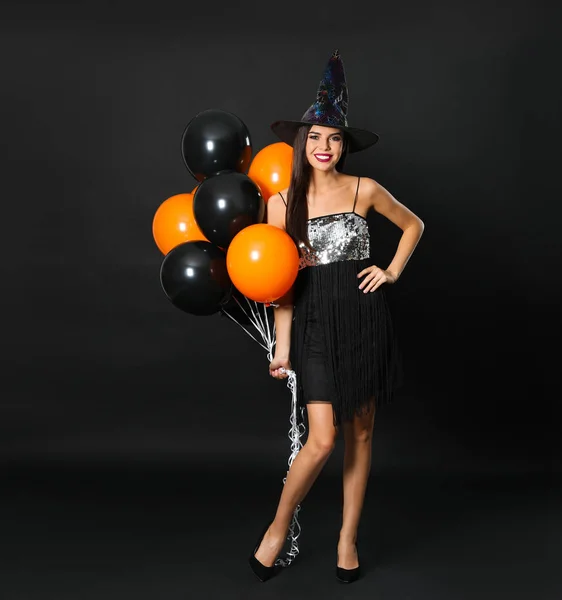 Hermosa mujer con traje de bruja con globos para la fiesta de Halloween sobre fondo negro —  Fotos de Stock