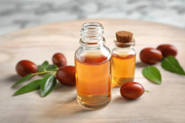 Bouteilles en verre avec huile de jojoba et graines sur table lumineuse — Photo