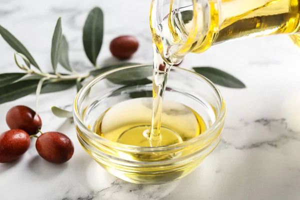 Verter con aceite de jojoba de la jarra en un tazón sobre una mesa de mármol blanco — Foto de Stock