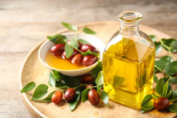 Glass bottle with jojoba oil and seeds on wooden table — Stock Photo, Image