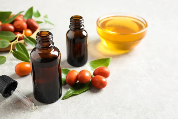 Bouteille en verre avec huile de jojoba et graines sur table en pierre grise. Espace pour le texte — Photo