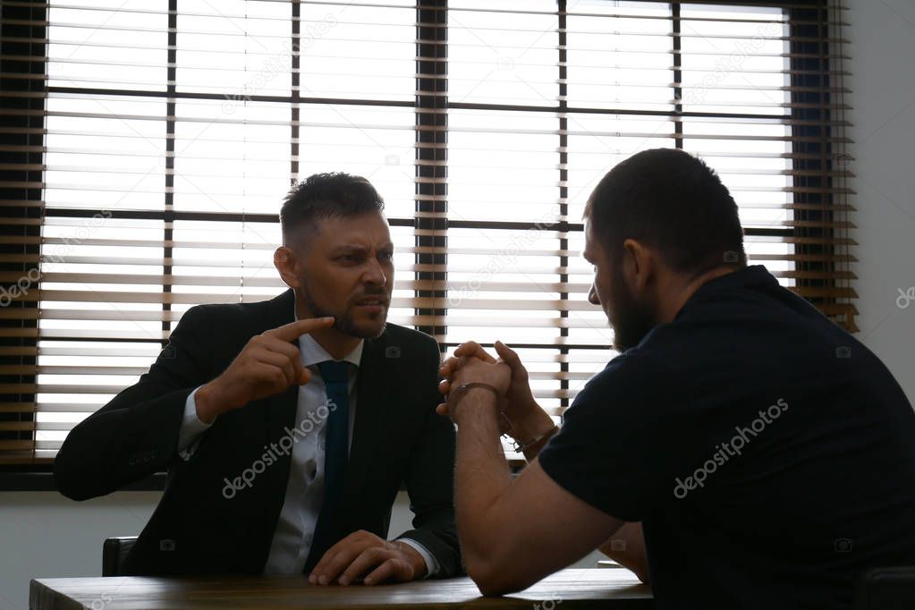 Angry detective interviewing criminal in interrogation room