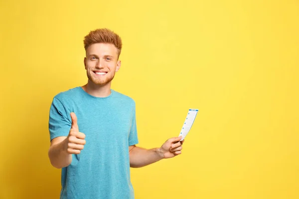 Портрет счастливого молодого человека с лотерейным билетом на желтом фоне — стоковое фото