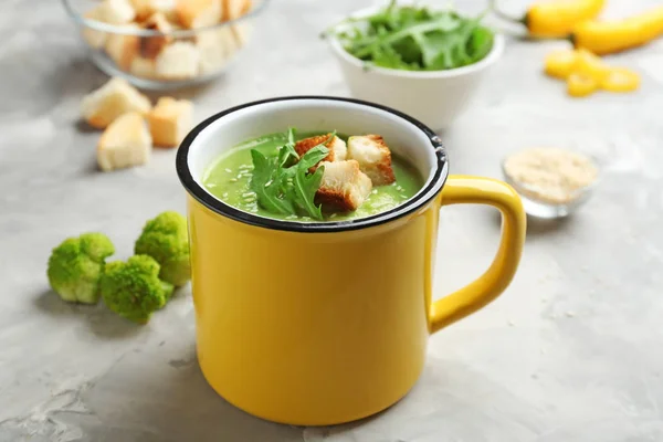 Metal mug of broccoli cream soup with croutons served on grey table — Stock Image Metal mug of broccoli cream soup with croutons served on grey table Stock Image