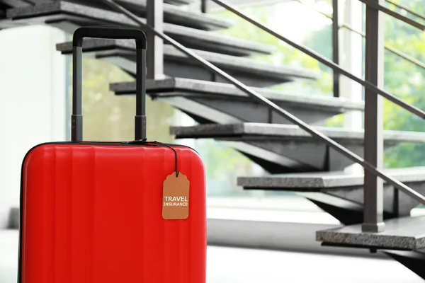 Maleta roja con etiqueta de SEGURO DE VIAJE en escaleras interiores, espacio para texto — Foto de Stock