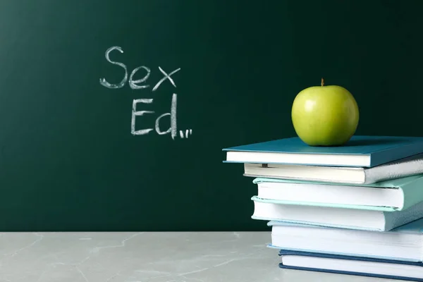 Libros y manzana sobre mesa gris cerca de pizarra con frase "Sex ed " — Foto de Stock