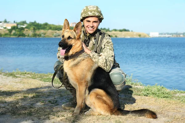 Hombre en uniforme militar con perro pastor alemán cerca del río — Foto de Stock