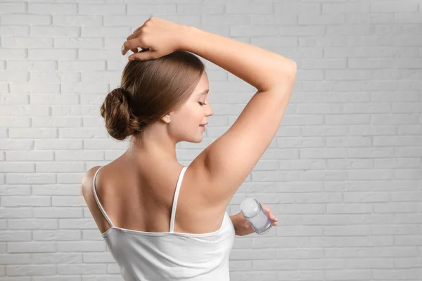 Mujer joven aplicando desodorante de alumbre de cristal a la axila contra la pared de ladrillo —  Fotos de Stock