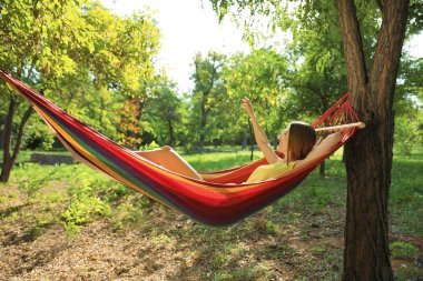 Genç bayan yeşil bahçedeki hamakta dinleniyor.