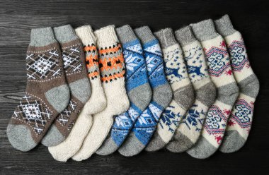 Different knitted socks on black wooden background, flat lay clipart