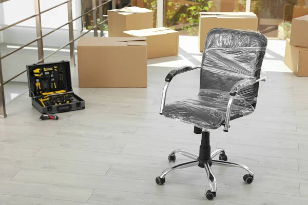 Židle zabalená ve filmu a zabalené věci v kanceláři, prostor pro text. Přesouvání služby — Stock fotografie