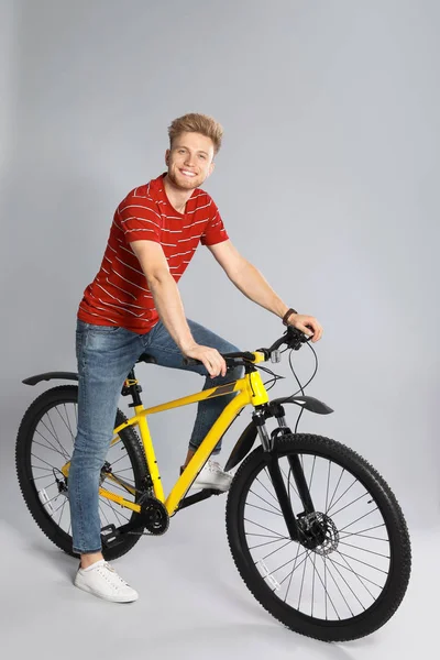 Schöner junger Mann mit Fahrrad auf grauem Hintergrund — Stockfoto