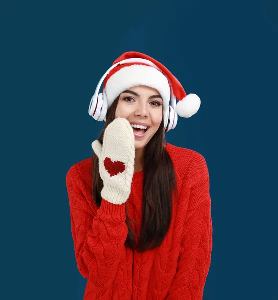 Mujer joven en Santa Sombrero escuchando música navideña sobre fondo azul oscuro —  Fotos de Stock