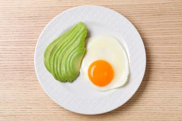 Bord gebakken ei en avocado op houten tafel, bovenaanzicht. Gezond ontbijt — Stockfoto