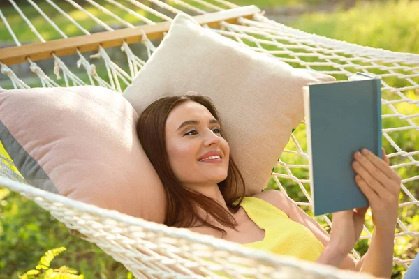 Młoda kobieta czyta książkę w wygodnym hamaku w zielonym ogrodzie — Zdjęcie stockowe
