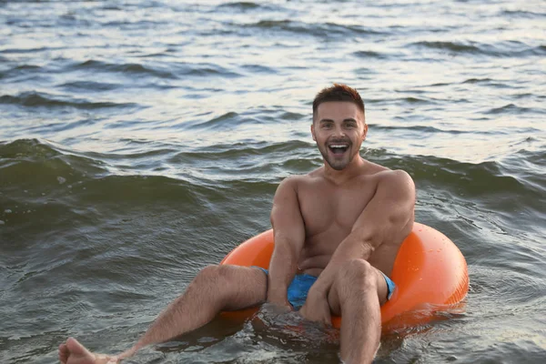 Glücklicher junger Mann auf aufblasbarem Ring im Wasser — Stockfoto