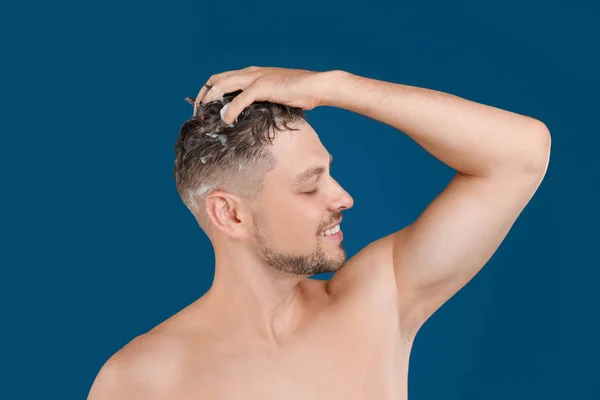 Schöner Mann wäscht Haare auf blauem Hintergrund — Stockfoto