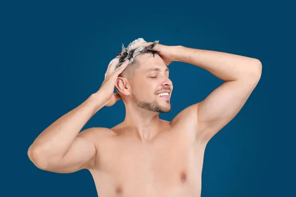 Красивий чоловік миє волосся на синьому фоні — стокове фото