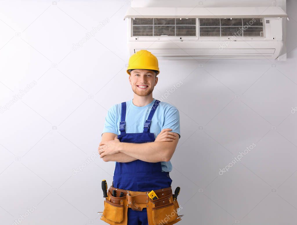 Professional technician near modern air conditioner indoors