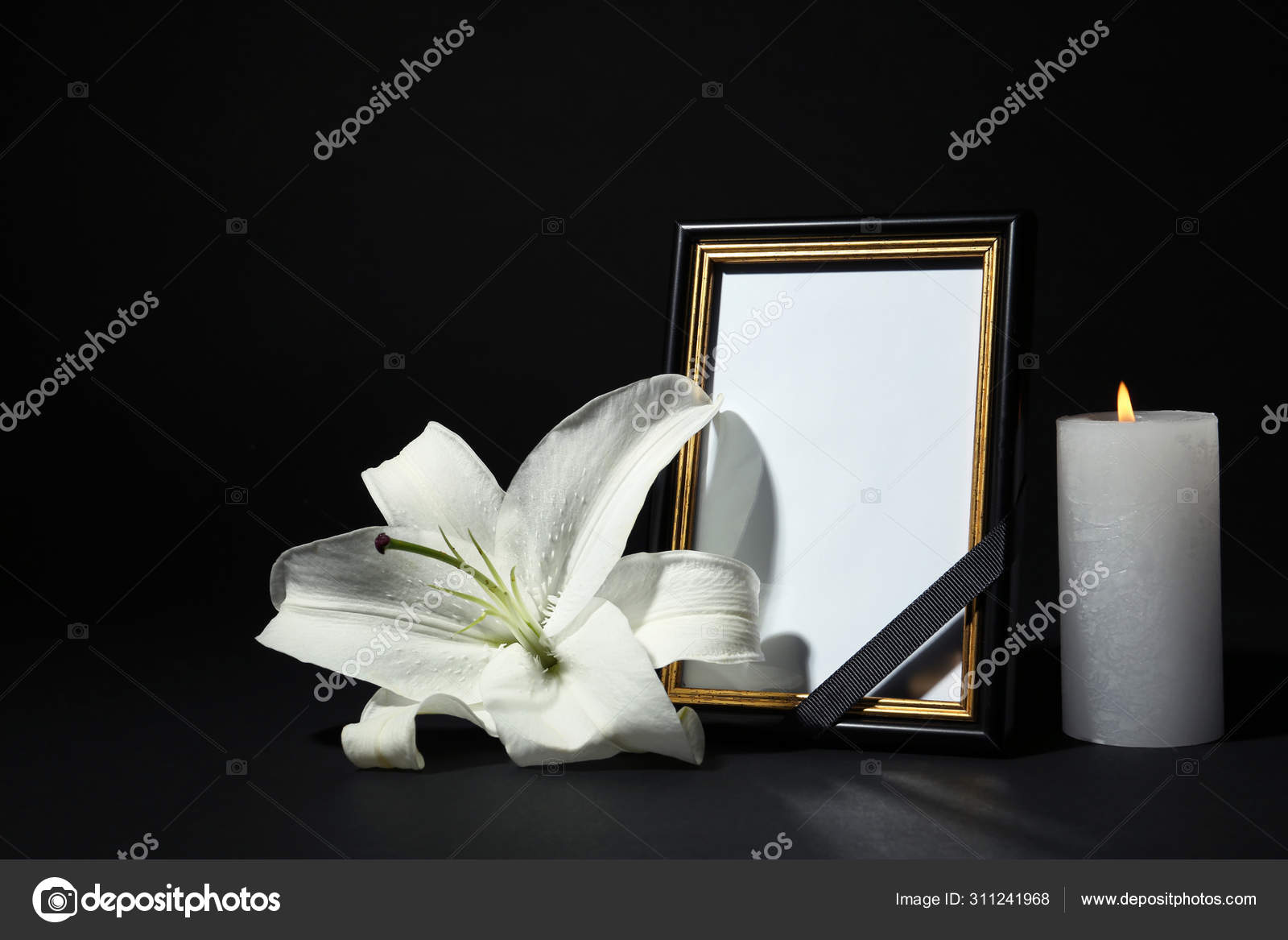 Funeral photo frame with ribbon, white lily and candle on dark table