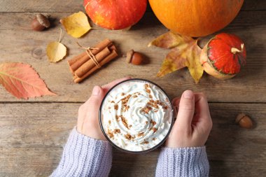 Ahşap masada elinde cam bardak, lezzetli balkabağı aromalı latte tutan kadın.