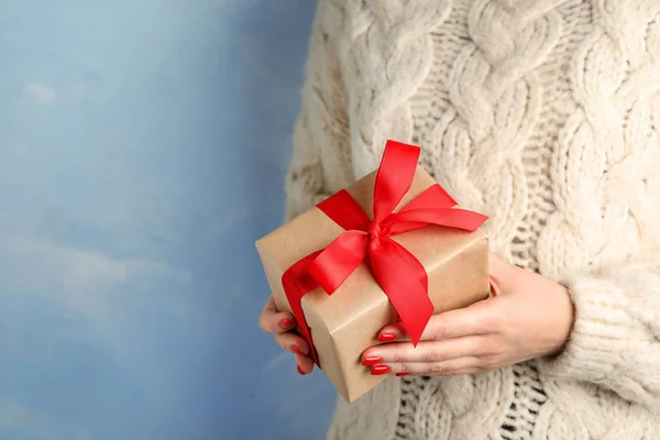 Молода жінка тримає різдвяний подарунок на синьому фоні, крупним планом. Простір для тексту — стокове фото