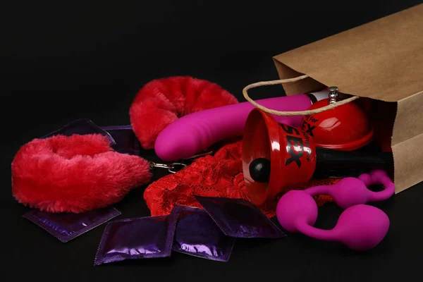 Saco de compras e brinquedos sexuais diferentes no fundo preto — Fotografia de Stock