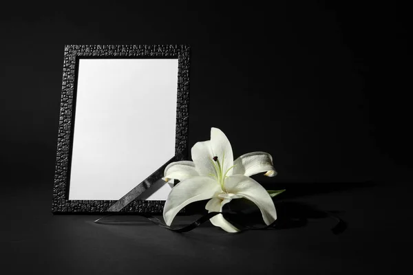 Funeral photo frame with ribbon and white lily on black background. Space for design