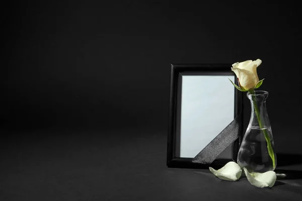 Funeral photo frame with ribbon and white rose on black background. Space for design