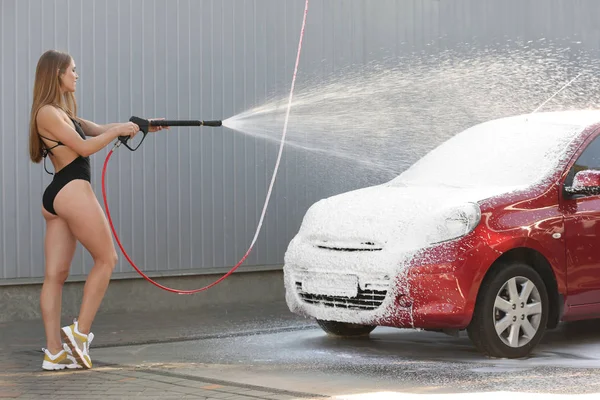 Young woman in swimsuit with high pressure water jet cleaning automobile at car wash — Stok fotoğraf