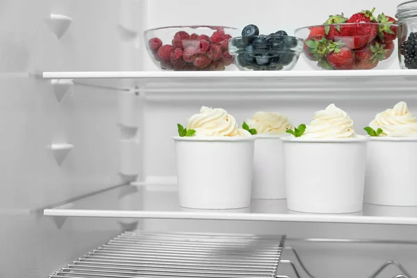 Cups with tasty frozen yogurt on fridge shelf